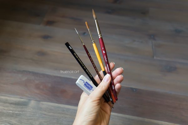 Oksana holding pencil, three brushes and eraser in her hand.