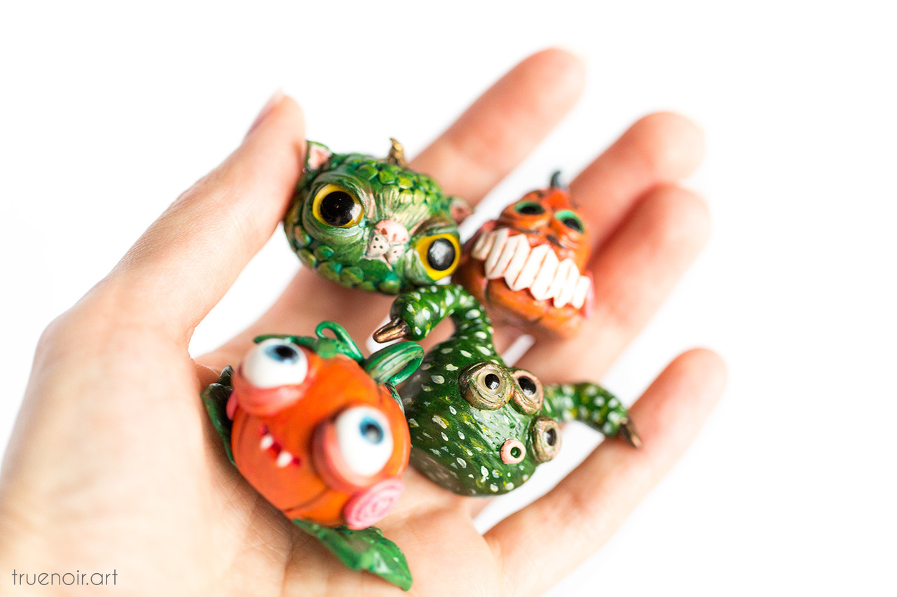 Four orange pumpkin and green gourd monster figurines in a hand.