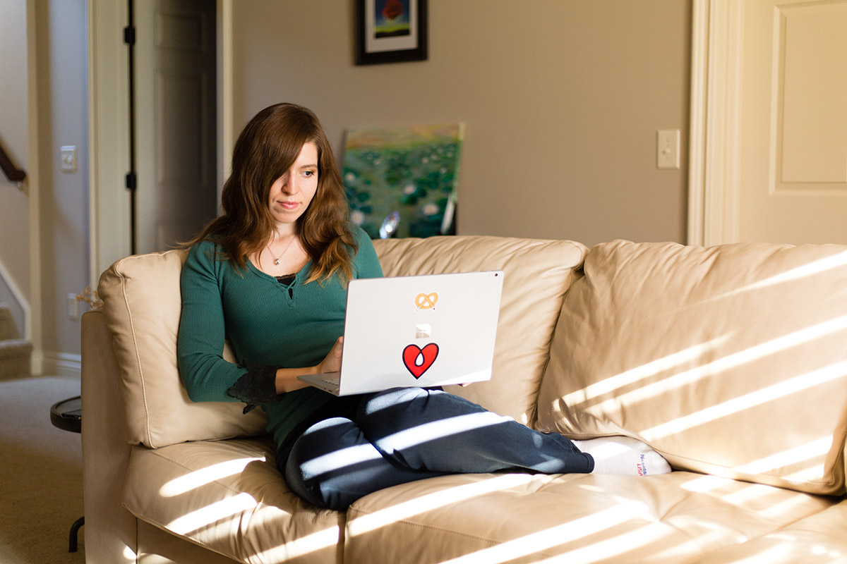 Oksana sitting on a couch with a laptop. There are a bunch of bring sunrays crossing the interior from the right. side